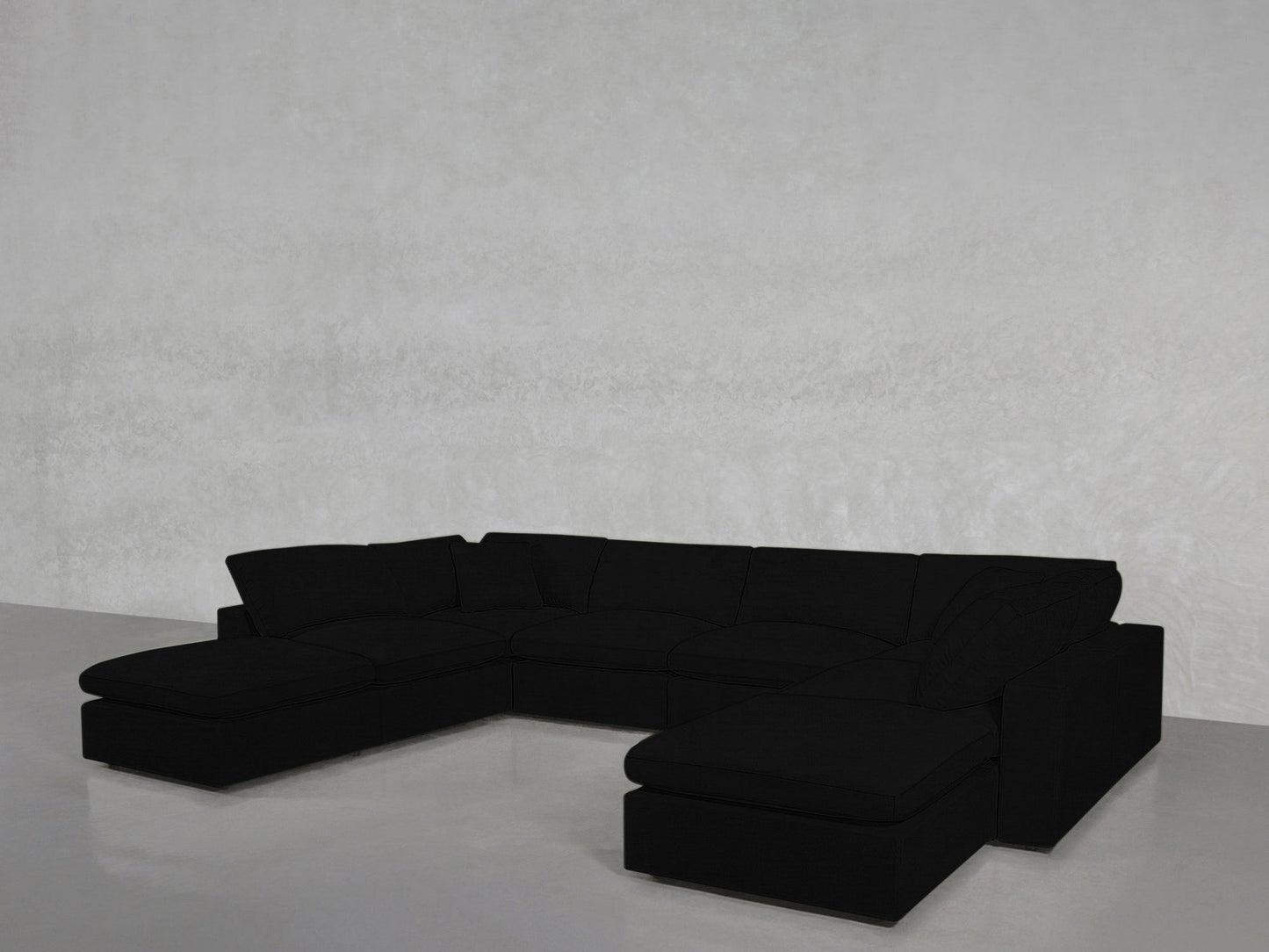 An 8-Seat Modular Double Lounger U-Sectional with plush black cushions sits in an empty room featuring light gray walls and a smooth, light gray floor.