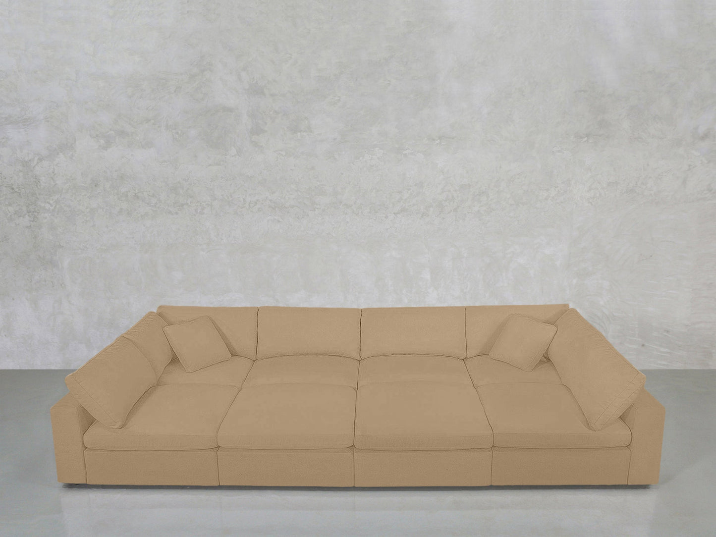 An 8-Seat Modular Pit in beige with matching cushions is placed against a light gray textured wall on a smooth, reflective floor.
