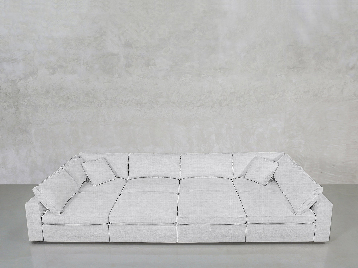 An 8-Seat Modular Pit sectional in light gray with wide seats and four matching cushions sits against a textured light gray wall on a polished concrete floor.