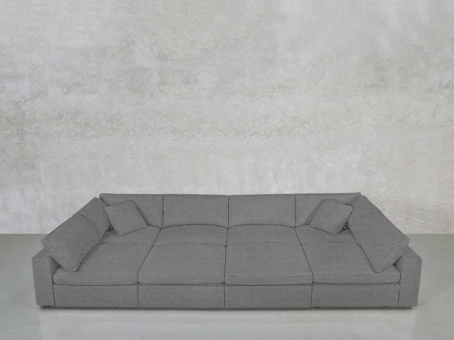The 8-Seat Modular Pit features a modern grey design with three seat cushions, wide armrests, and four matching throw pillows, set against a light textured wall and floor.