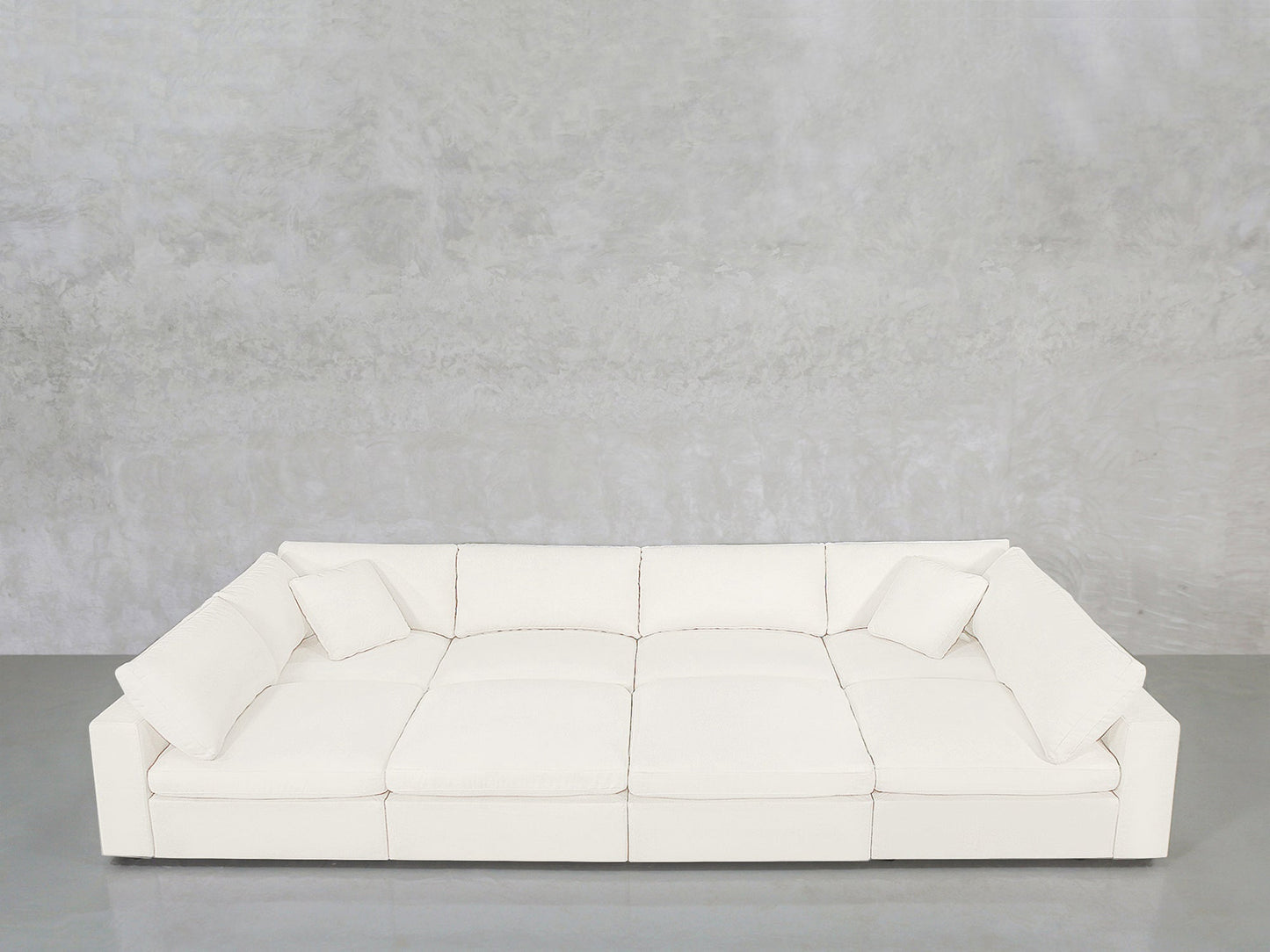The 8-Seat Modular Pit features a modern white design with three seat cushions and four matching square pillows, set against a light gray textured wall and a polished gray floor.