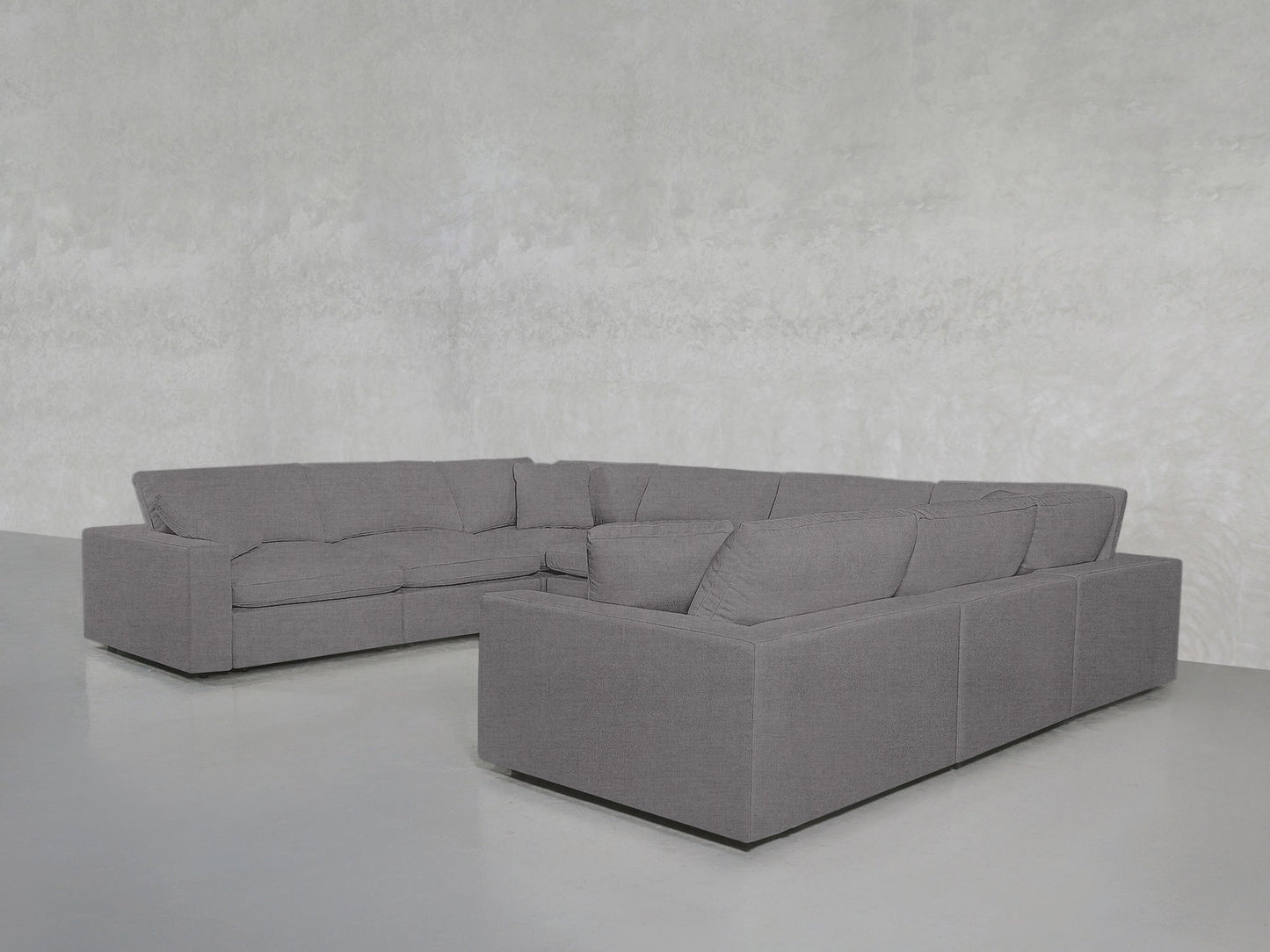 An 8-Seat Modular U-Sectional upholstered in light gray fabric is arranged in a minimalist room with pale gray walls and a smooth, light-colored floor.