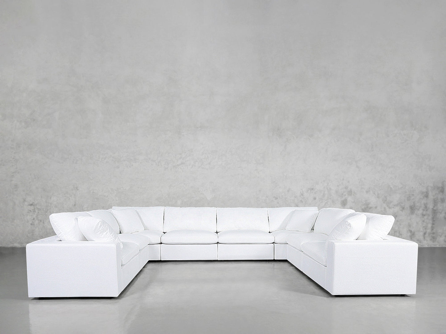 An 8-Seat Modular U-Sectional in white with cushions rests on a shiny, light gray floor against a plain, textured gray wall.