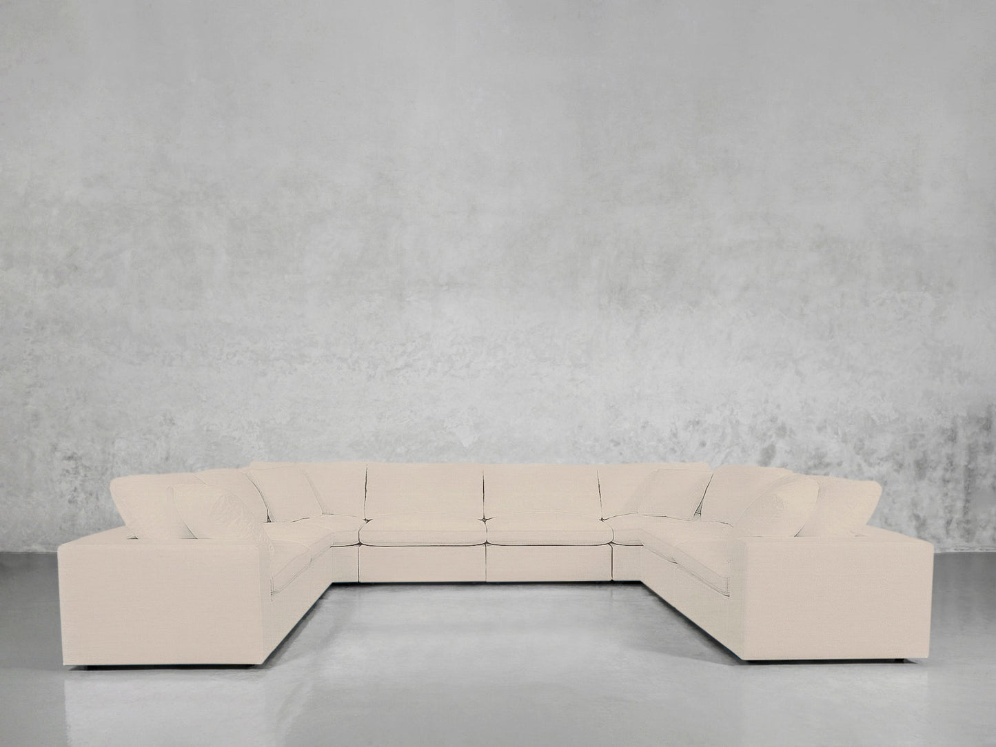 An 8-Seat Modular U-Sectional, large and modern with clean lines in light beige, is arranged in an empty room featuring light gray textured walls and a polished concrete floor.