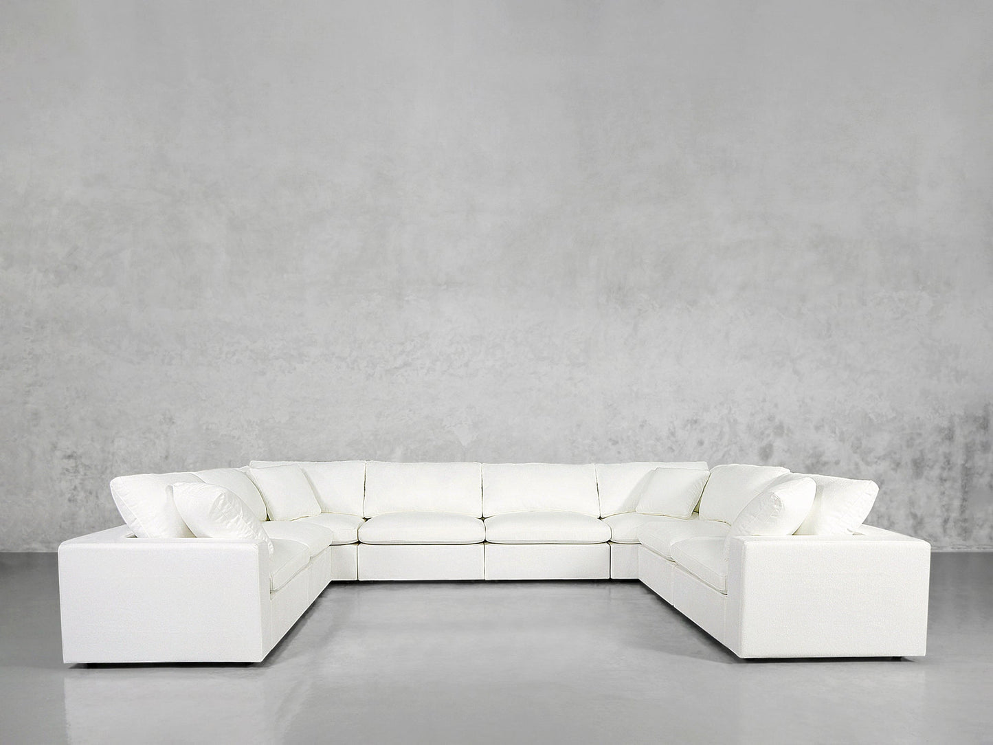An 8-Seat Modular U-Sectional with matching cushions is arranged against a plain, light gray wall and floor in a minimalist, modern room.