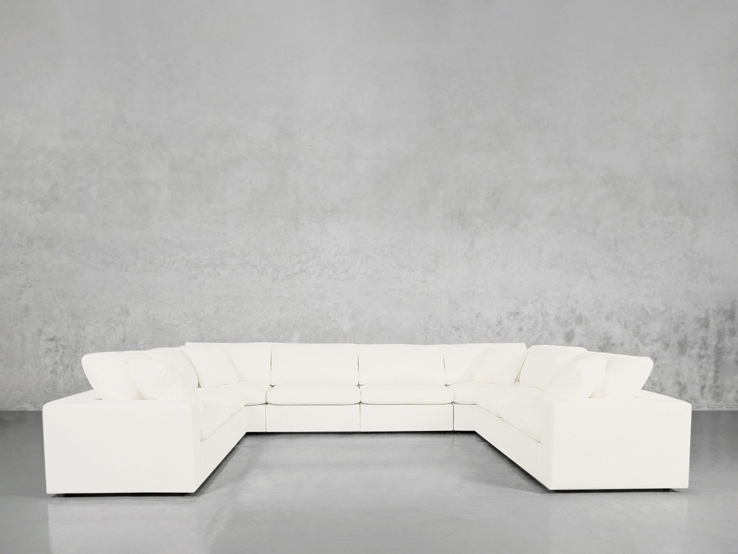 An 8-Seat Modular U-Sectional with clean, modern lines is arranged in an empty room featuring a concrete floor and a light gray textured wall.