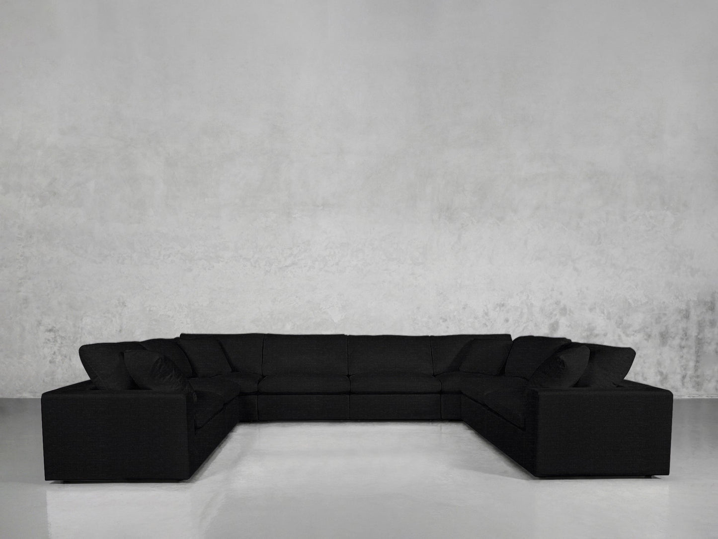 An 8-Seat Modular U-Sectional in black sits against a plain, light gray textured wall in a minimalist room with a glossy, light-colored floor.
