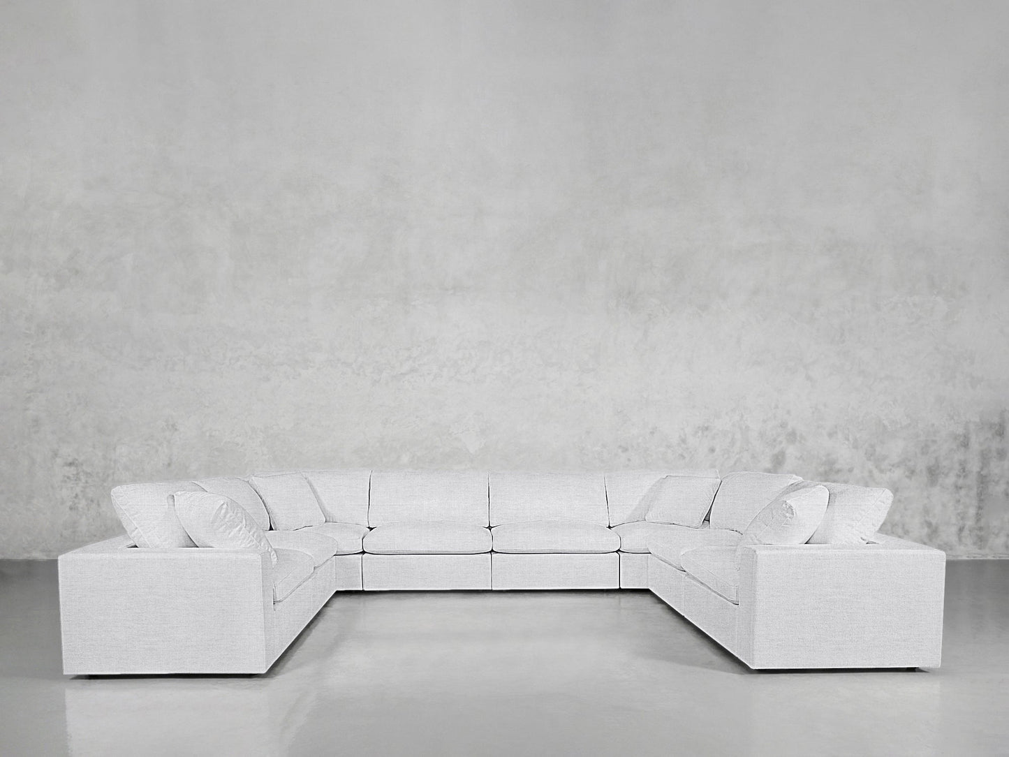 The 8-Seat Modular U-Sectional is a large, modern light gray sofa with multiple cushions, arranged in a U-shape against a textured gray wall and glossy floor.