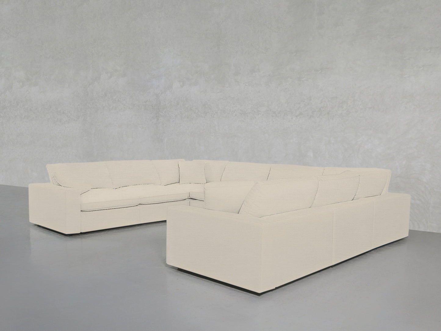 An 8-Seat Modular U-Sectional in light beige with clean lines and deep cushions sits in a minimalistic room featuring light gray concrete floors and textured light gray walls.