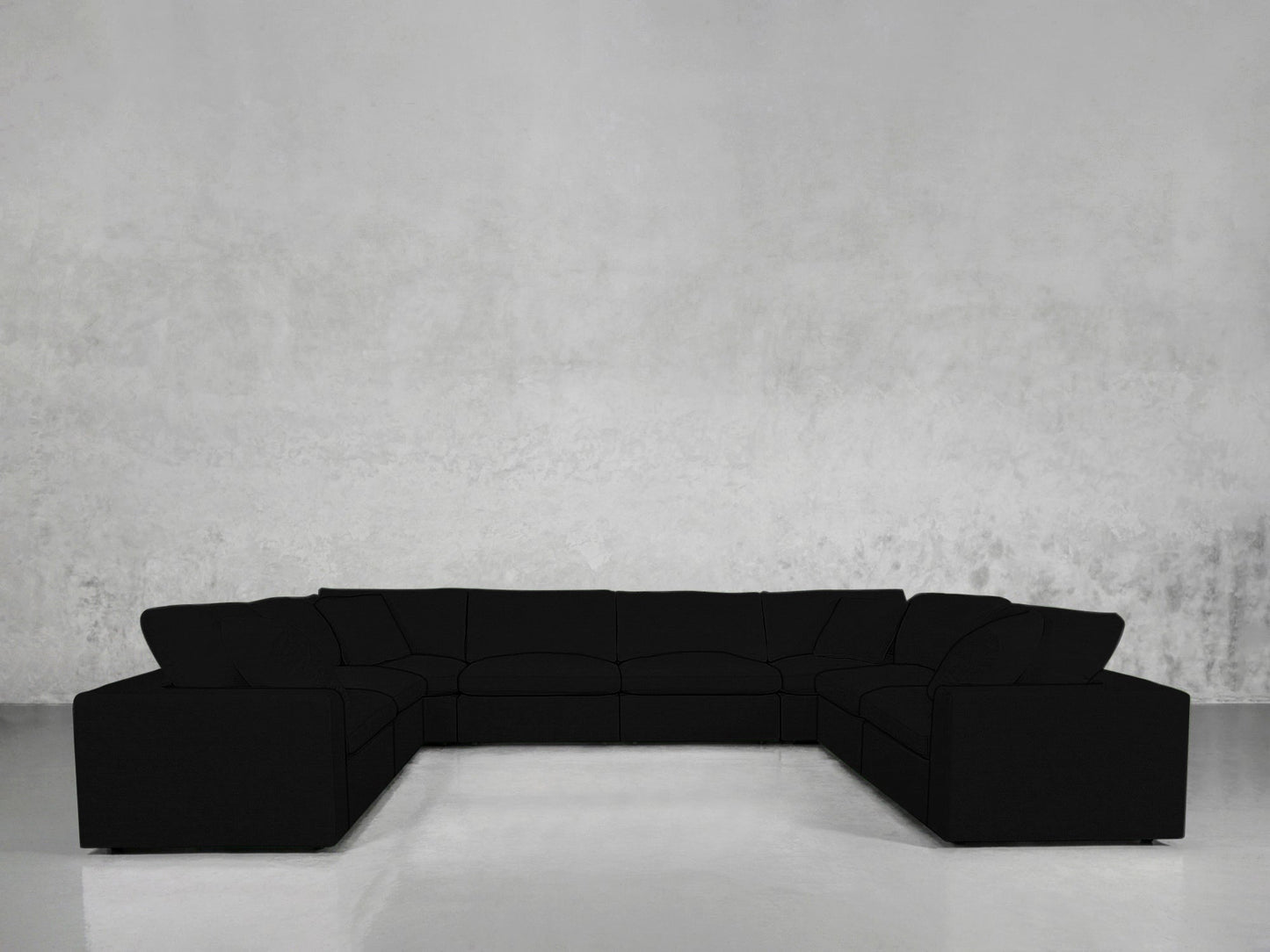 An 8-Seat Modular U-Sectional with plush black cushions is arranged in a U-shape against a plain, light grey textured wall in a minimalist room with a glossy floor.