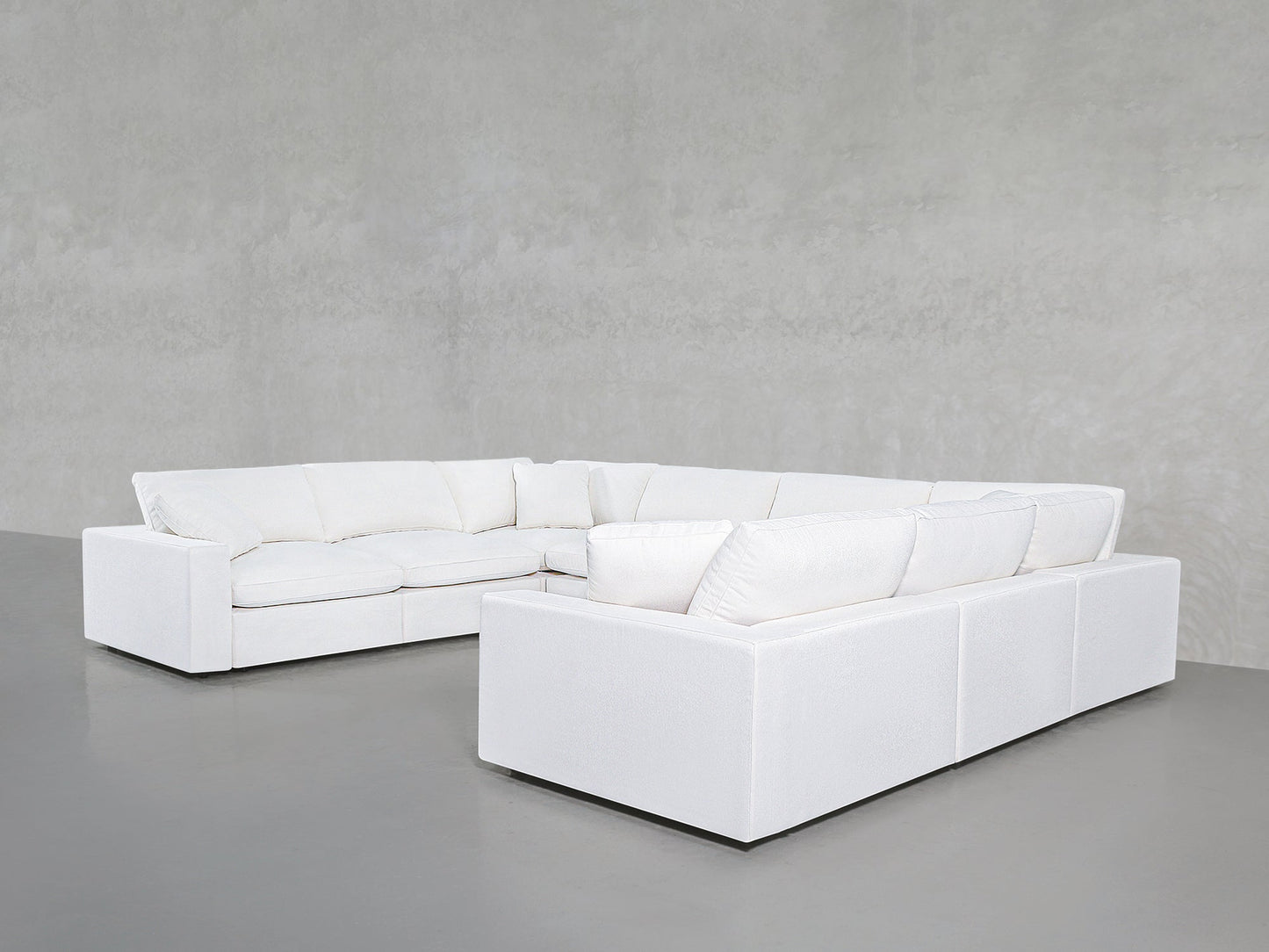 An 8-Seat Modular U-Sectional in modern white with deep cushions sits in the corner of a minimalist room with gray walls and a smooth gray floor.