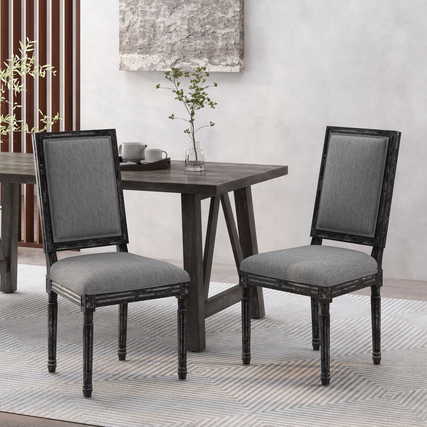 Two French Country Style Dining Chairs with upholstered seating and fluted legs in gray sit by a dark wooden dining table, topped with a small plant and cups, creating a modern, minimalistic dining space.
