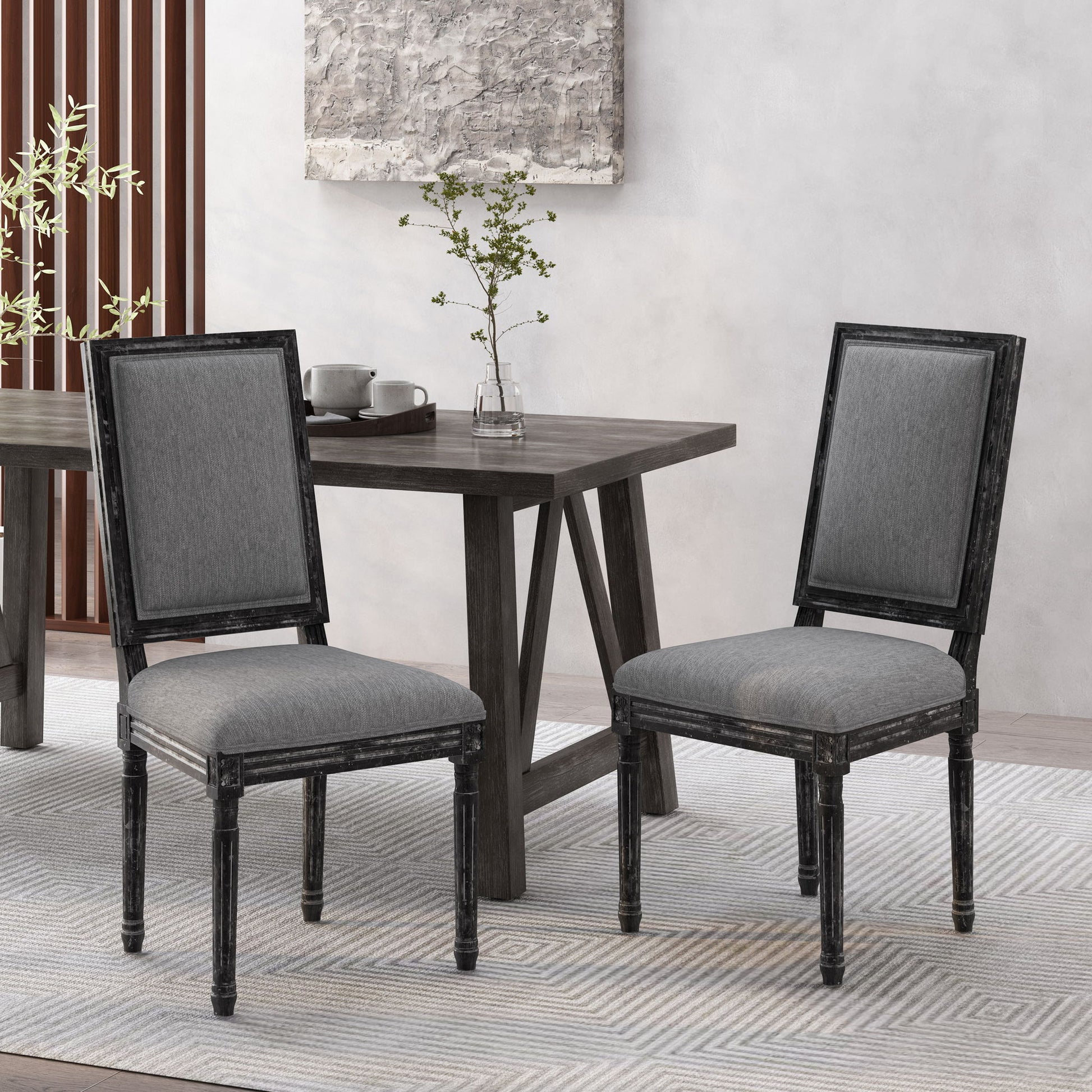 Two French Country Style Dining Chairs with upholstered seating and fluted legs in gray sit by a dark wooden dining table, topped with a small plant and cups, creating a modern, minimalistic dining space.