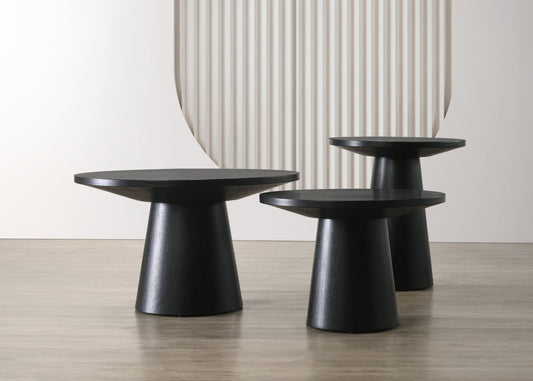 The Jasper 3 Piece Coffee, End, and Console Table set in Ebony Black is displayed on a light wood floor with a white wall and textured, curved backdrop.