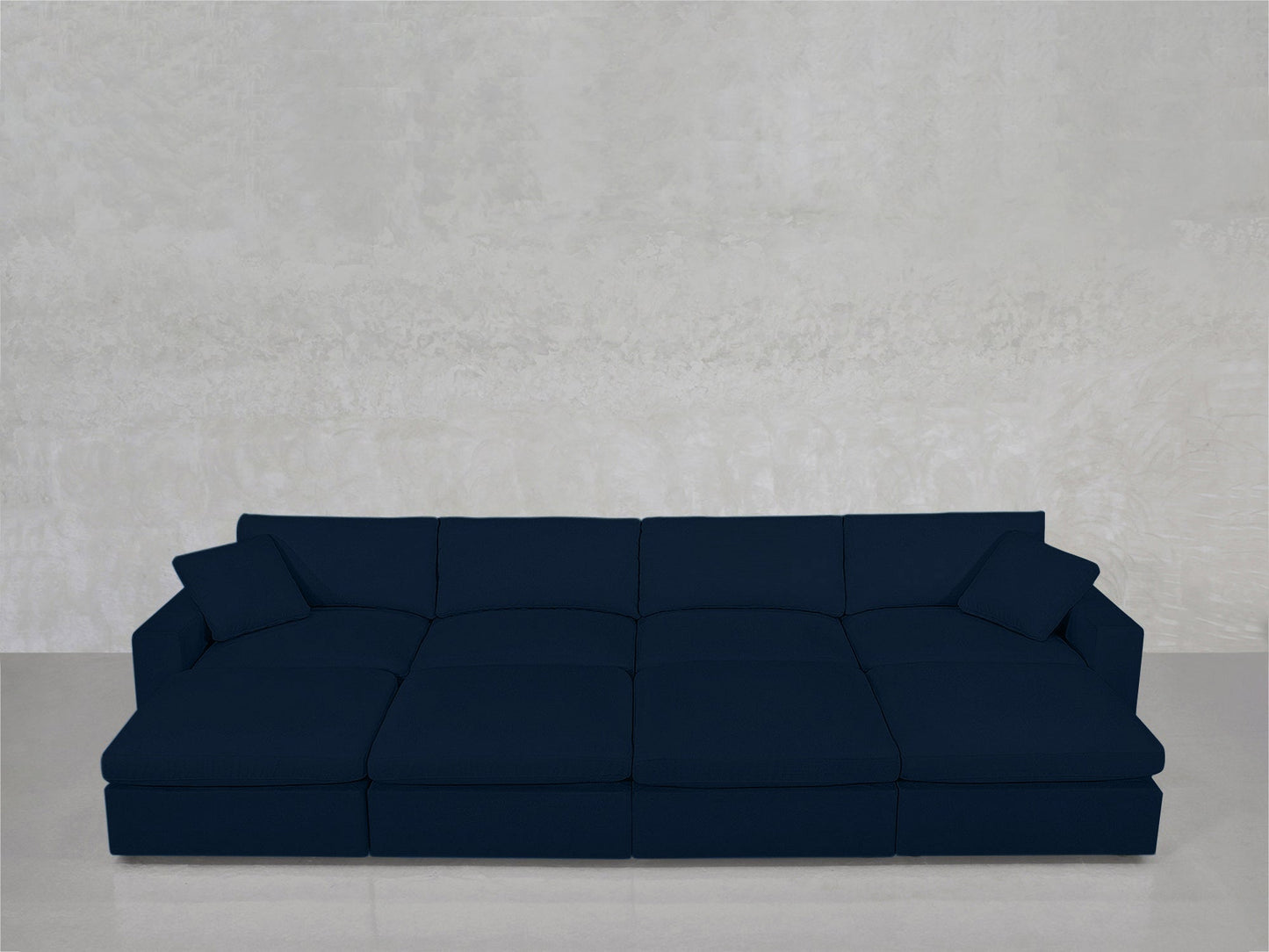 An 8-Seat Modular Daybed in dark blue, with two matching cushions, sits against a light gray textured wall on a glossy floor.