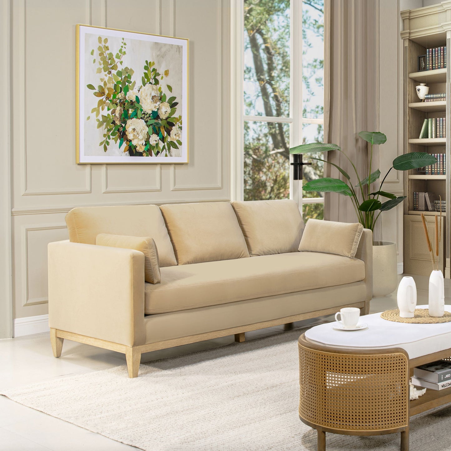 The Knox - Modern Farmhouse Sofa with matching cushions sits in a bright living room featuring a large window, framed floral art, a green plant, and a round coffee table set with tea cups for a cozy, naturally lit atmosphere.