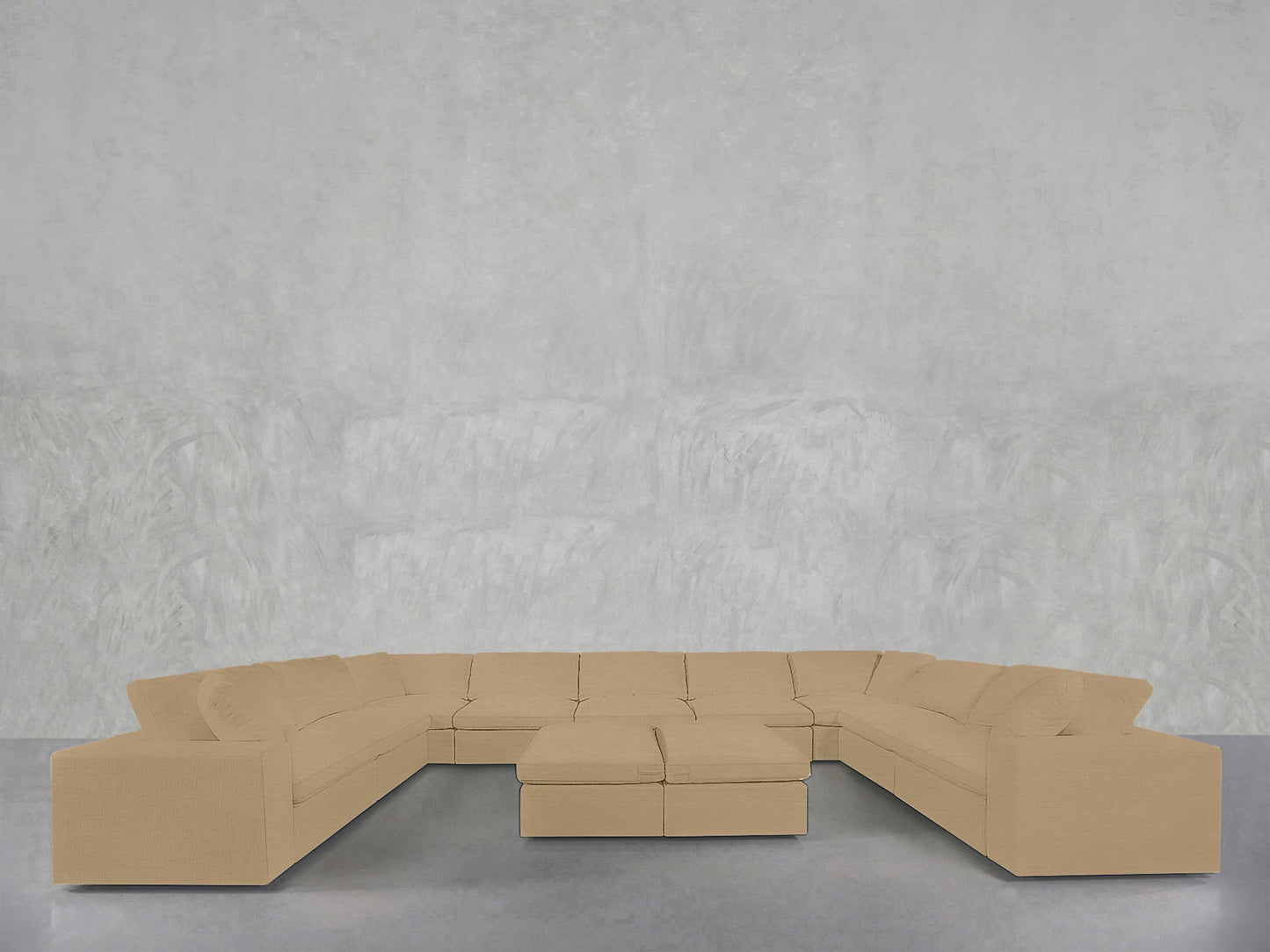 A 9-Seat Modular U-Sectional with Double Ottoman in beige is arranged on a smooth gray floor, set against a textured light gray wall.