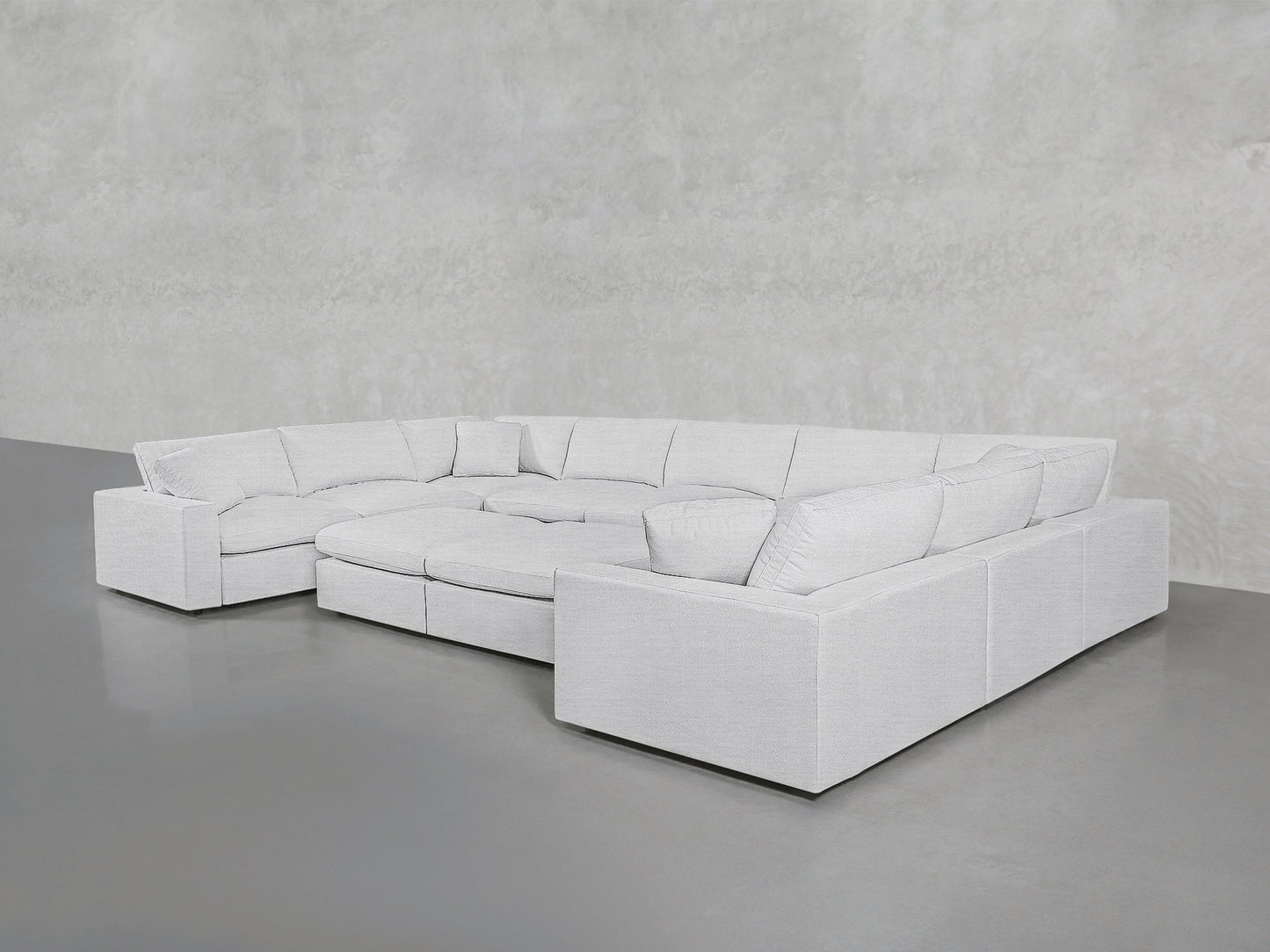 A spacious, modern 9-Seat Modular U-Sectional with Double Ottoman in light gray, featuring clean lines and plush cushions, is set against a plain light-colored wall on a smooth gray floor.
