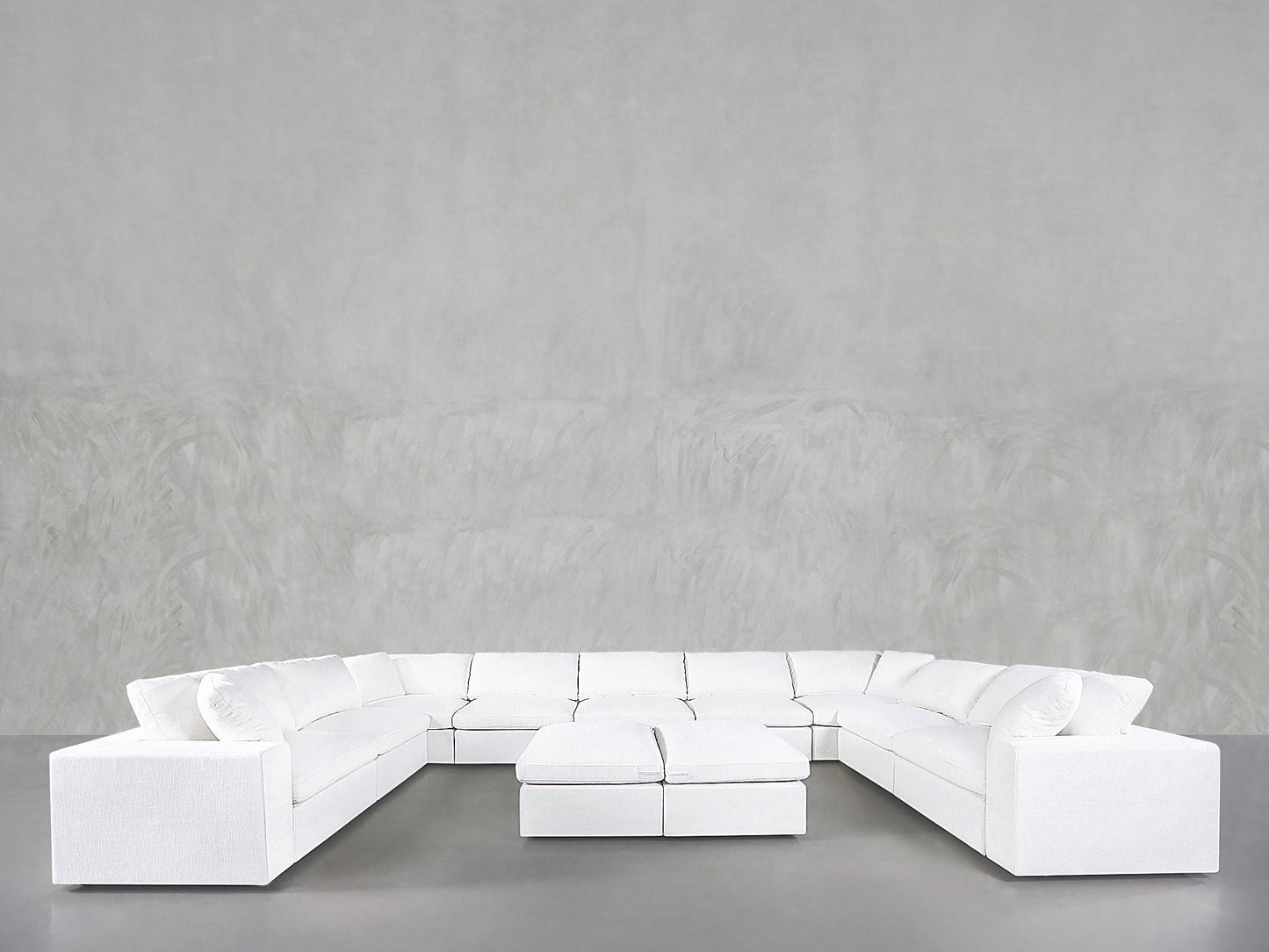 A 9-Seat Modular U-Sectional with Double Ottoman is set in a spacious room featuring smooth, light gray walls and a gray floor.