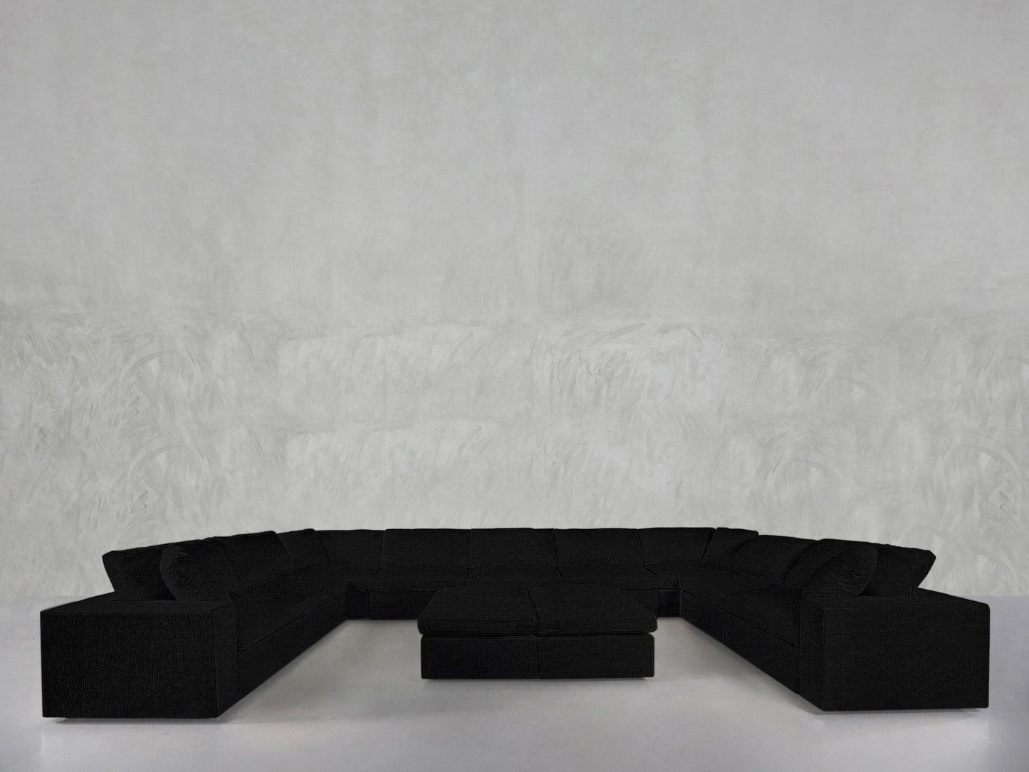 A 9-Seat Modular U-Sectional with Double Ottoman in black stands against a light gray textured wall in a minimalistic room featuring a white floor.