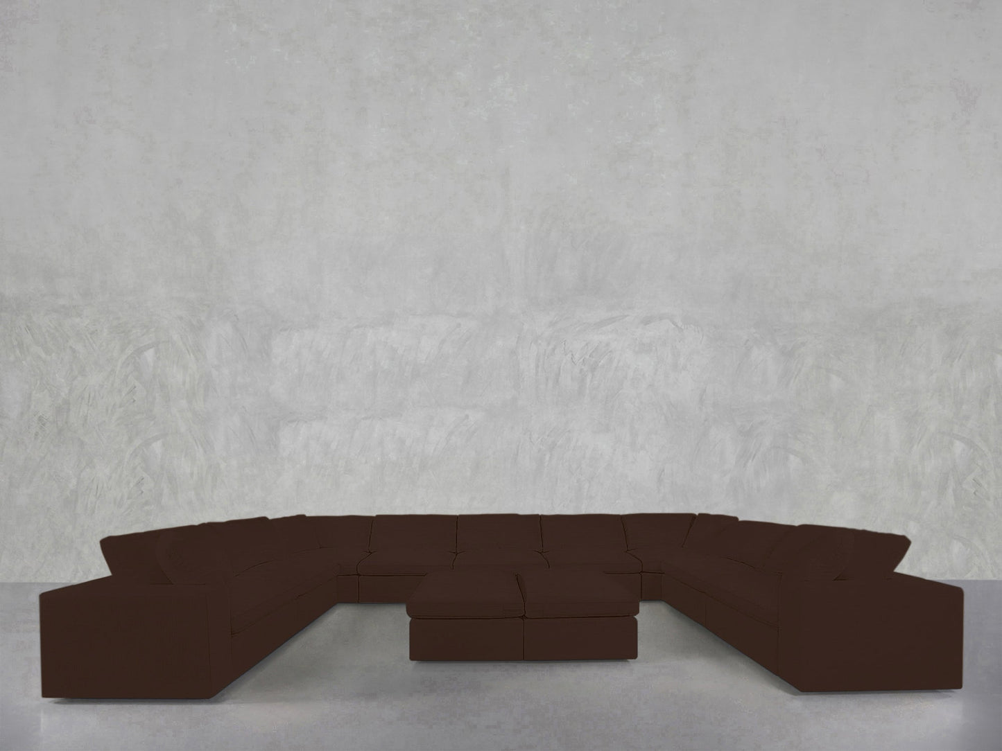 A 9-Seat Modular U-Sectional with Double Ottoman in dark brown sits against a plain light gray textured wall in a minimalist room with a smooth floor.