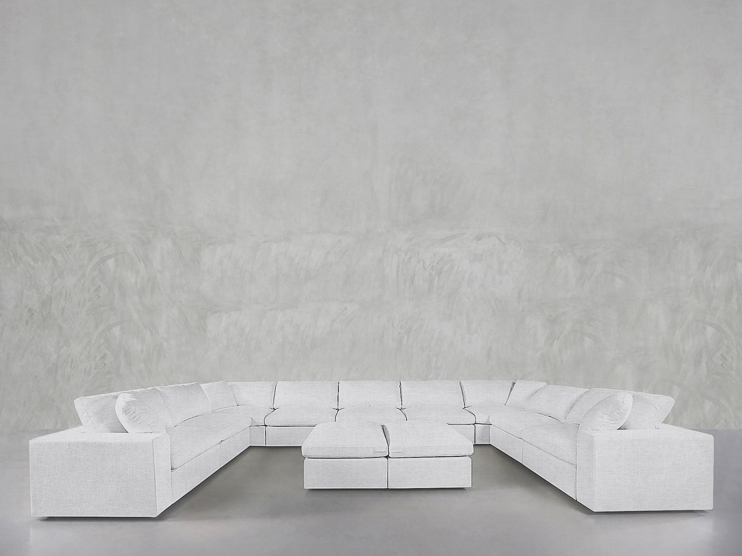 Spacious, modern 9-Seat Modular U-Sectional with Double Ottoman in light gray, displayed against a plain, textured light gray wall and floor.