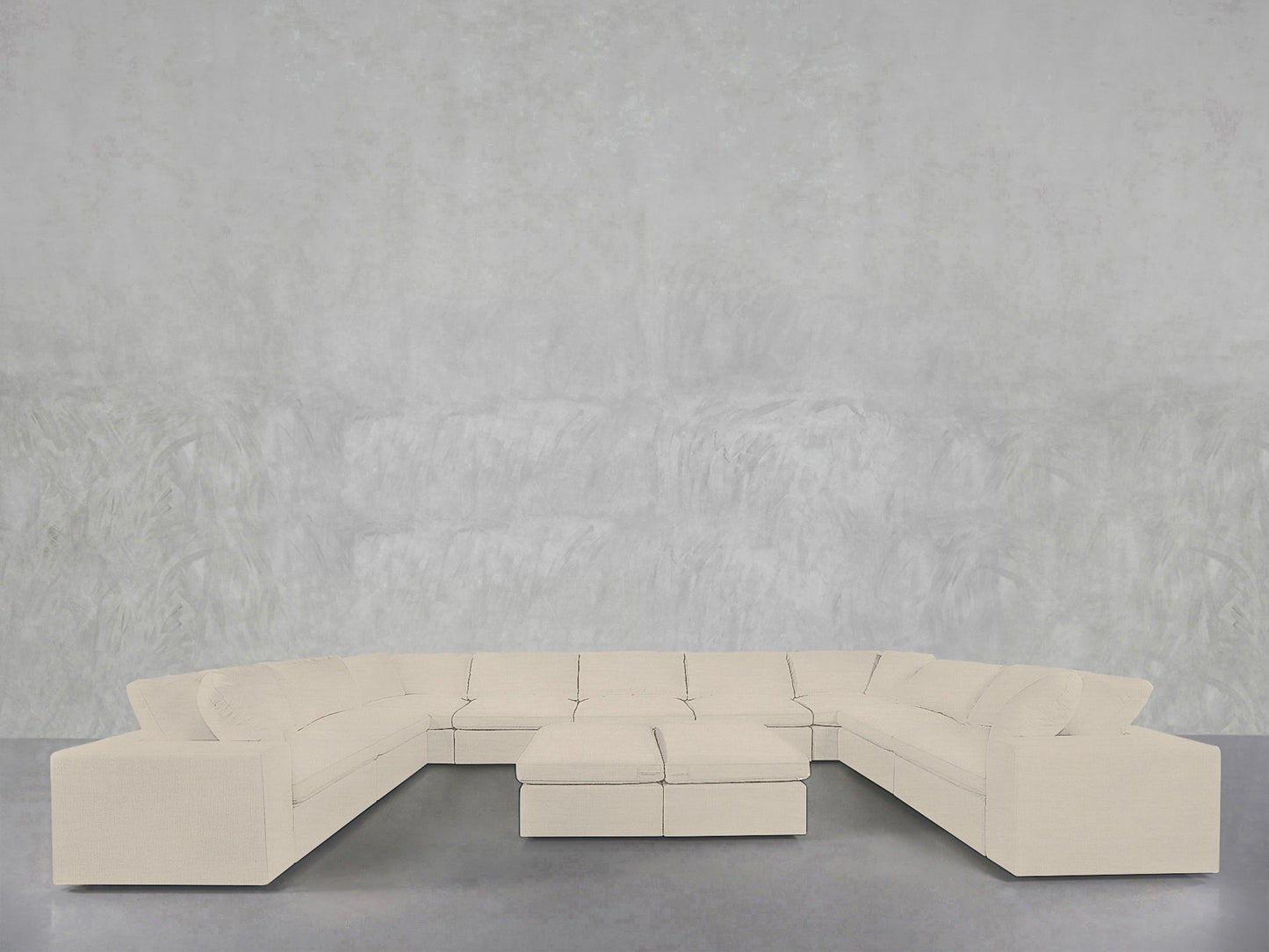 The 9-Seat Modular U-Sectional with Double Ottoman, in light beige, is arranged in a U-shape against a minimalist light gray textured wall and smooth gray floor.