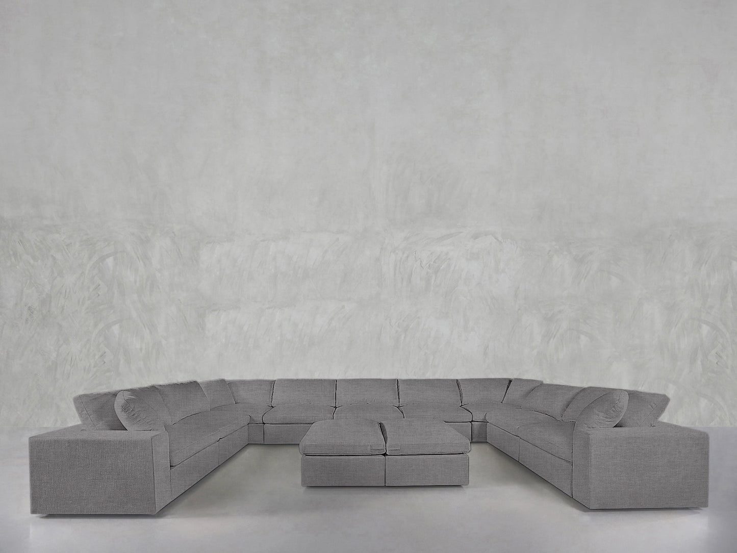 A spacious, modern gray 9-Seat Modular U-Sectional with double ottomans features wide arms and sits before a plain, light gray textured wall.