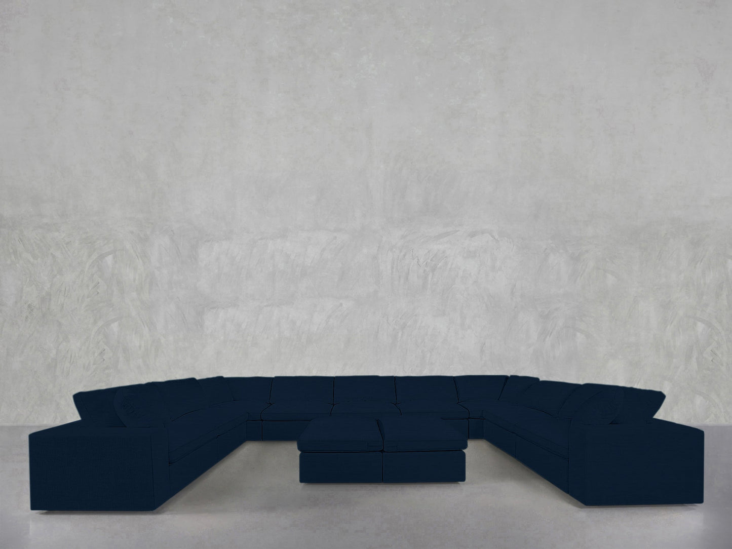 A 9-Seat Modular U-Sectional with Double Ottoman in dark blue is placed against a plain, light gray textured wall and floor.