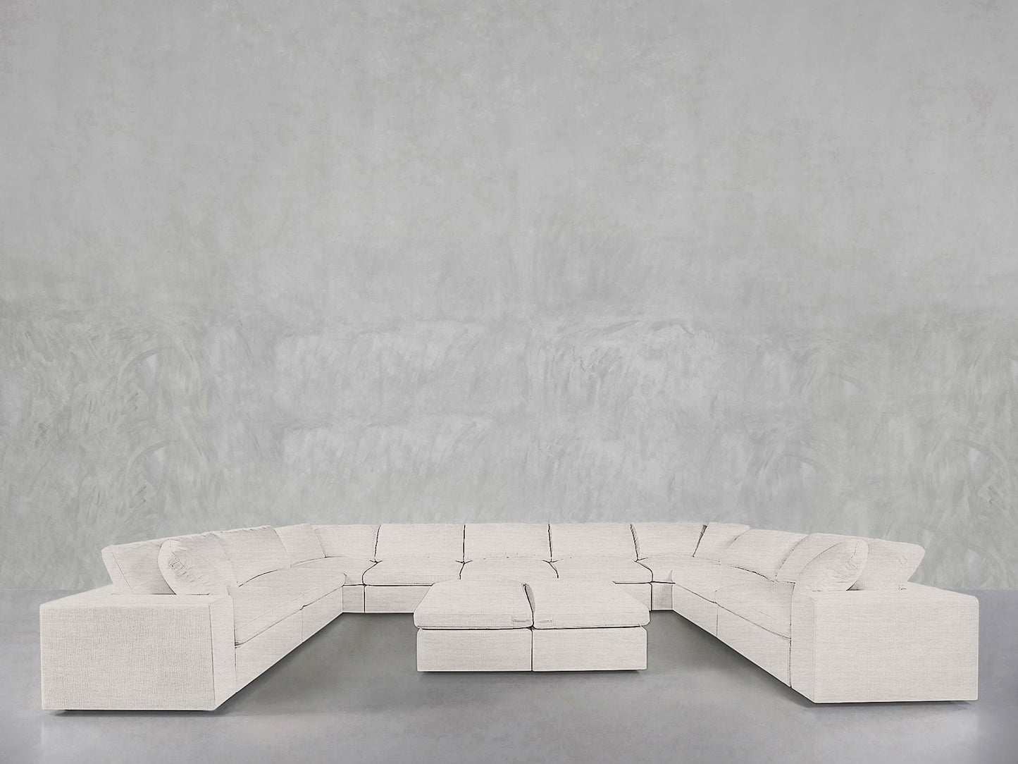 The 9-Seat Modular U-Sectional with Double Ottoman in light beige fabric is arranged around its two matching ottomans, set against a minimalist gray wall and floor.
