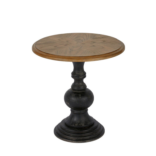 The Table With Reclaimed - Natural is a small round side table with a light wood top displaying a subtle starburst pattern and a dark, ornate pedestal base.