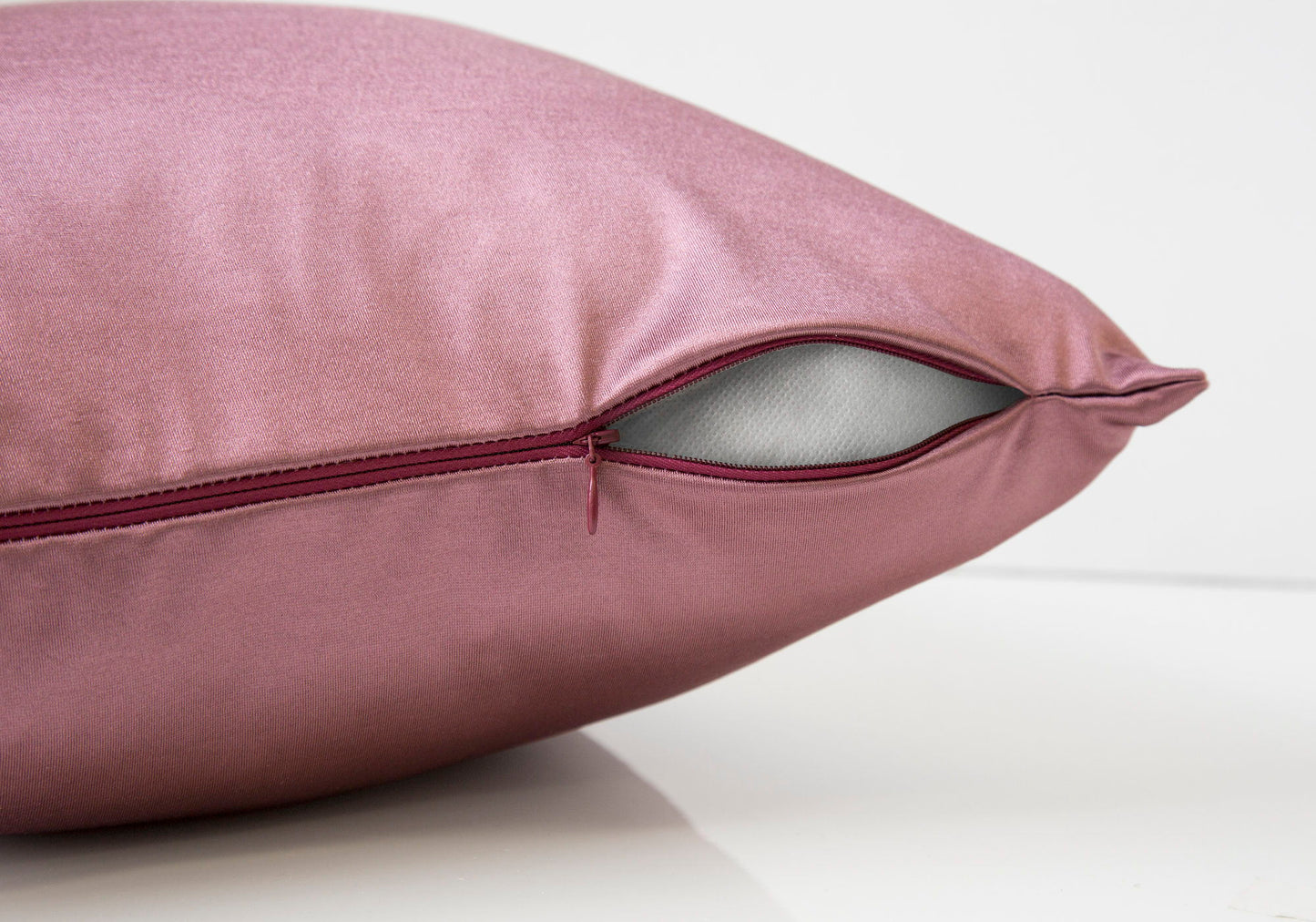 A close-up of a pink satin decorative throw pillow (square, insert included), with a partially open zipper revealing the hypoallergenic inner stuffing. The background is plain white for a modern look.