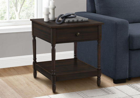 The Accent - Table, 2 Tier, Square, Traditional - Walnut sits by a blue sofa on a light wood floor. Sunlight streams in as books, decor pieces, and candles rest on its surface and lower shelf.