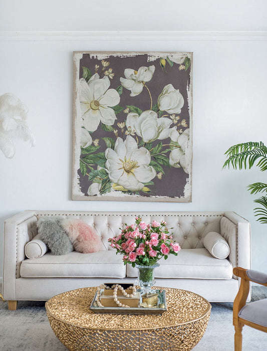A stylish living room with a white tufted sofa, colorful pillows, a round gold coffee table with pink roses, Large Botanical Wall Art Prints (White/Gray) on the wall, and a potted plant in the corner.