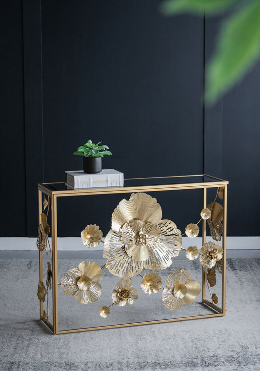 A Console Table With Mirrored Glass Top, Modern Entryway Table For Living Room Foyer Entryway - Gold stands against a dark wall, adorned with large gold flowers. A small potted plant and a stack of books rest on the table.