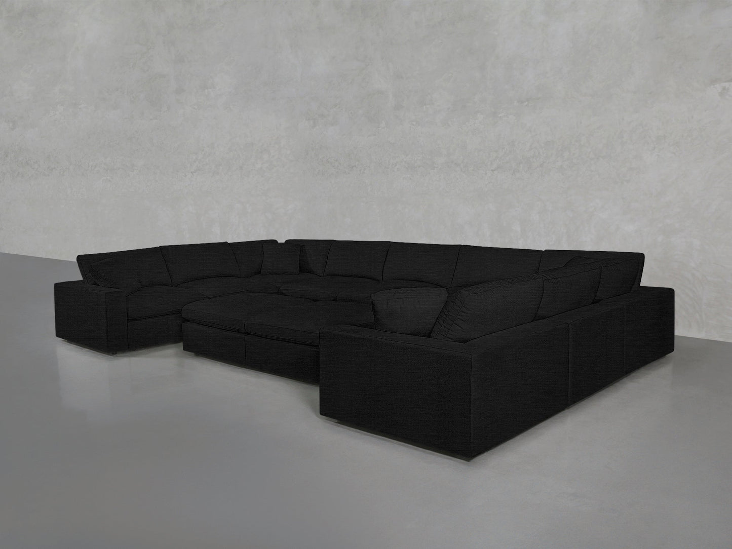 A spacious, modern 9-Seat Modular U-Sectional with Double Ottoman in black sits in an empty room with light gray walls and a smooth gray floor.