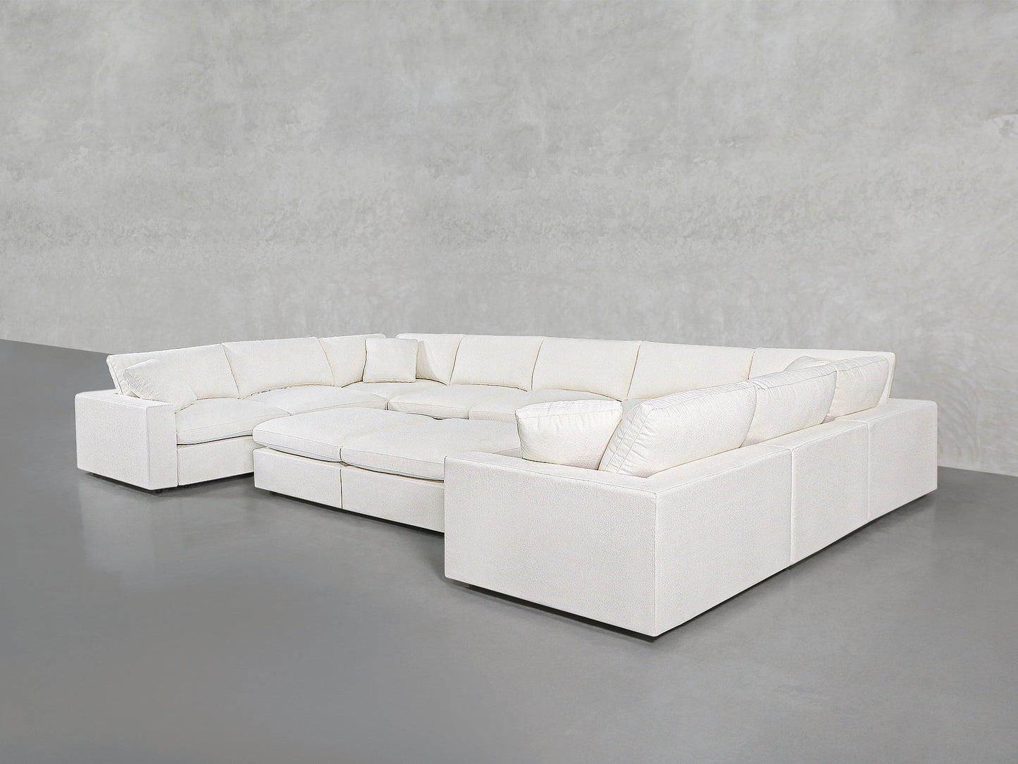 A spacious 9-Seat Modular U-Sectional with Double Ottoman in modern white, featuring plush cushions, sits against a plain light gray wall and floor in a minimalist room.