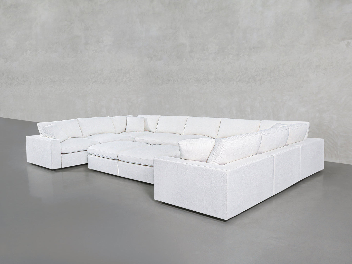 The 9-Seat Modular U-Sectional with Double Ottoman, in modern white with plush cushions, is arranged against a plain light gray wall and a smooth gray floor.
