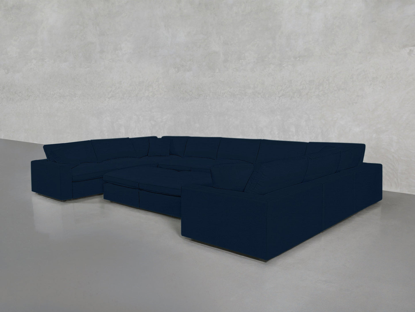 A 9-Seat Modular U-Sectional with Double Ottoman in dark blue sits on a smooth, light gray floor against a pale textured wall, featuring clean lines and deep cushions.