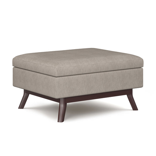 The Owen Upholstered Rectangular Storage Ottoman features a beige cushion top, dark wooden legs, and is displayed on a white background.