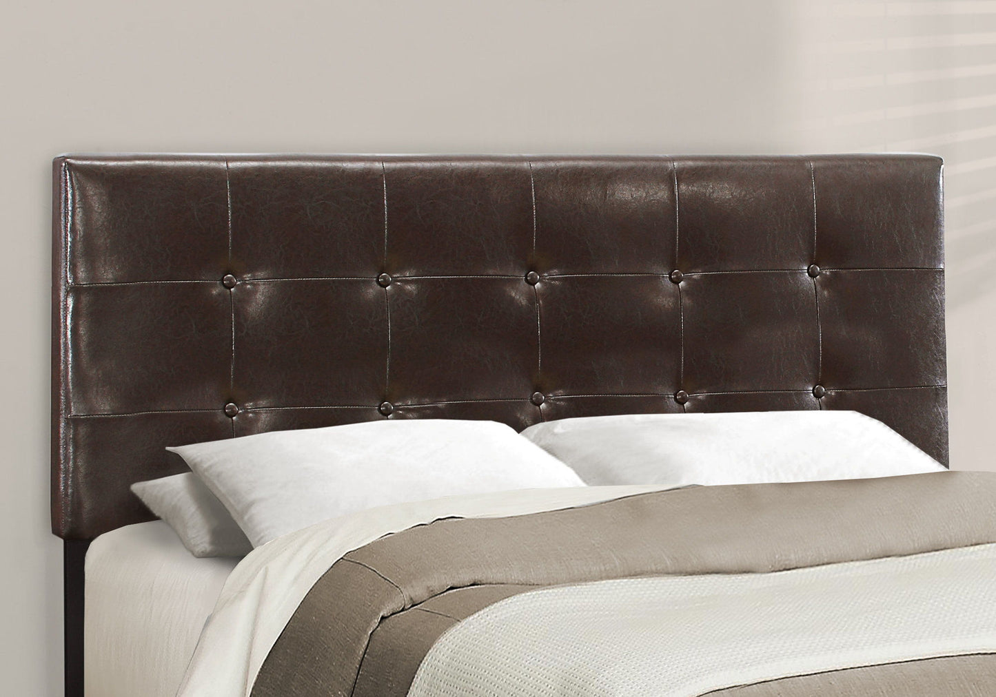 A transitional upholstered bed frame with a dark brown, tufted leather headboard and button accents, styled with white pillows and a beige and white quilt for a neutral look.