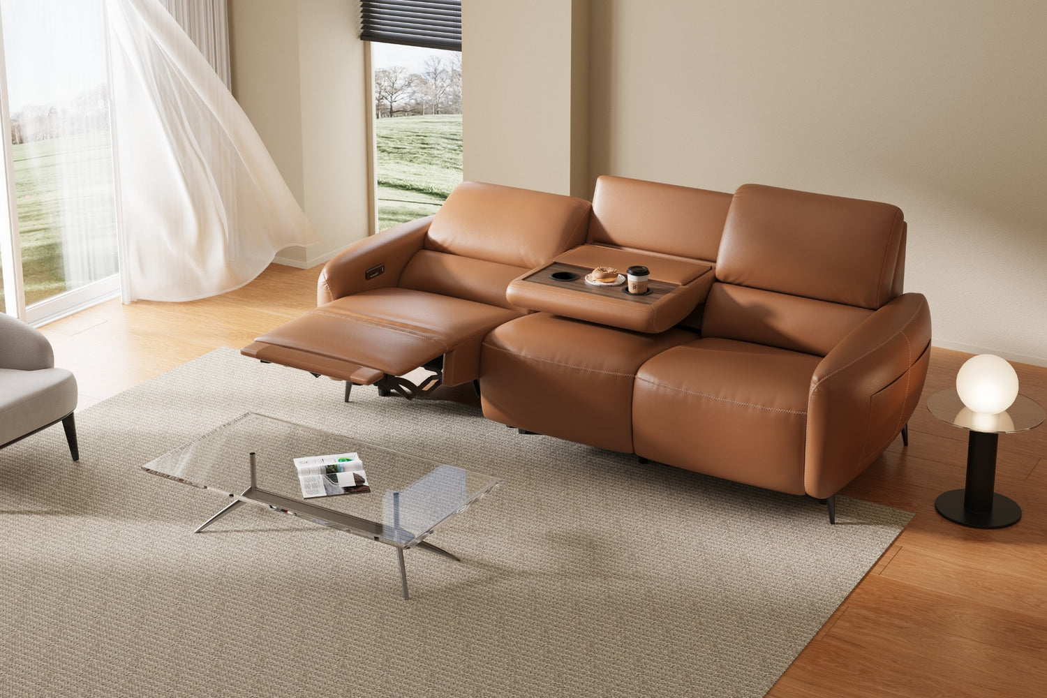 A modern living room with a brown reclining sofa featuring built-in cup holders. A glass coffee table with magazines is in front of it. A white curtain billows beside a large window, and a small round lamp is on the floor.