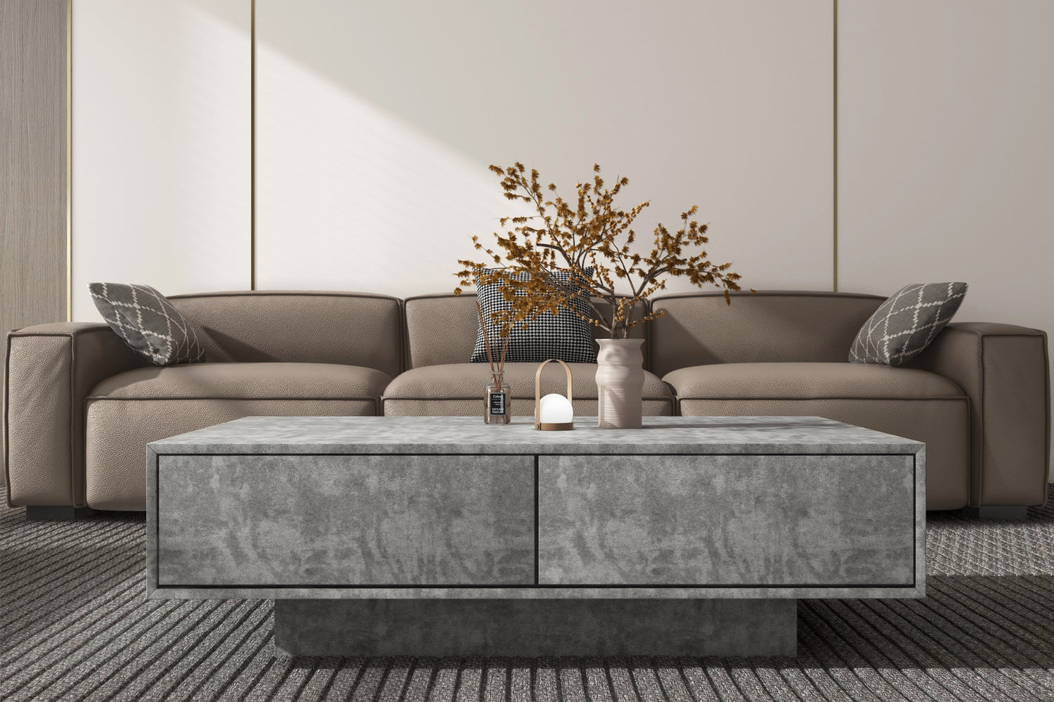 Modern living room with a gray sofa and decorative pillows. A large rectangular stone coffee table holds a small lamp, a vase with dried branches, and a candle. The room features neutral tones and minimalist design.