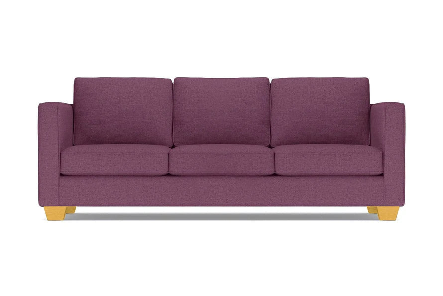 The Catalina Sofa, with its modern design in a purple hue, comes complete with three cushions. It features straight arms and light wooden legs, all showcased against a white background.