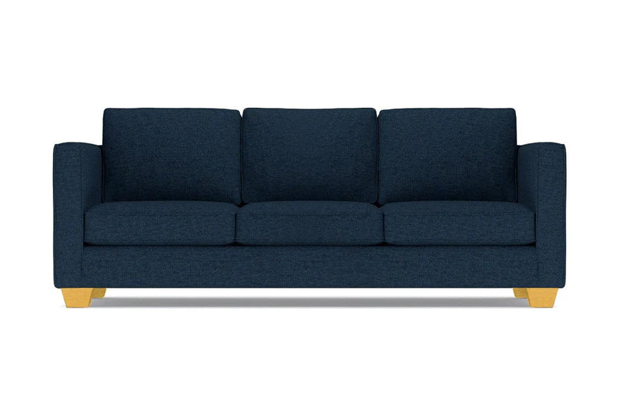 The Catalina Sofa is a dark blue three-seater featuring square cushions and light wooden legs, set against a white background.