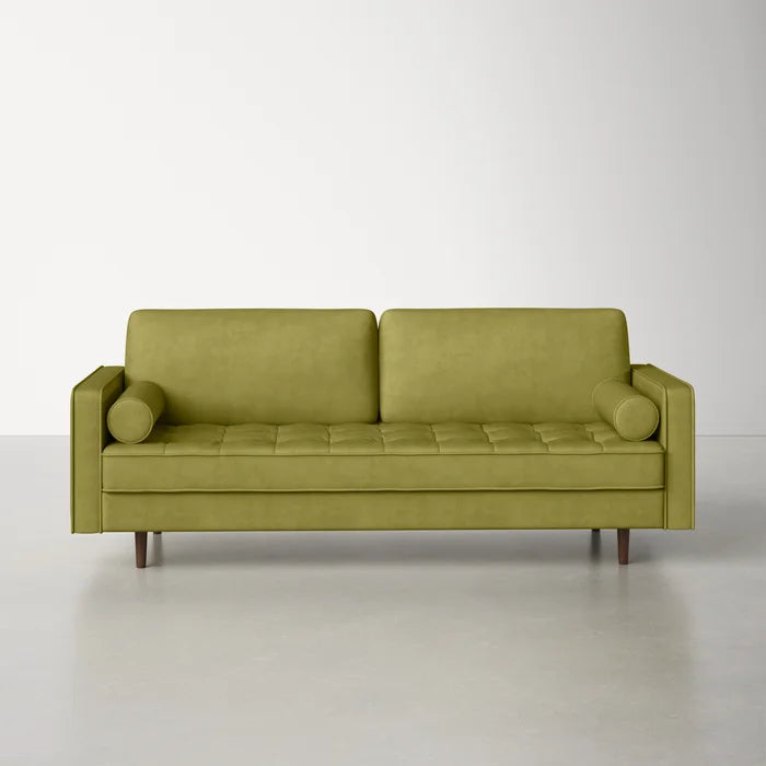 The Geo 84'' Upholstered Sofa, featuring tufted seat cushions, two bolster pillows, and wooden legs, is set against a plain off-white wall on a smooth gray floor.