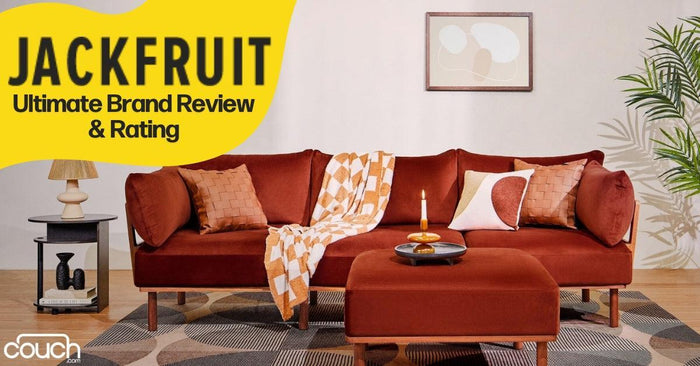 A cozy living room features a burnt orange sofa with decorative pillows and a patterned throw. In front sits a matching ottoman with a lit candle. The wall art and a potted plant complete the decor. Text reads "JACKFRUIT: Ultimate Brand Review & Rating.