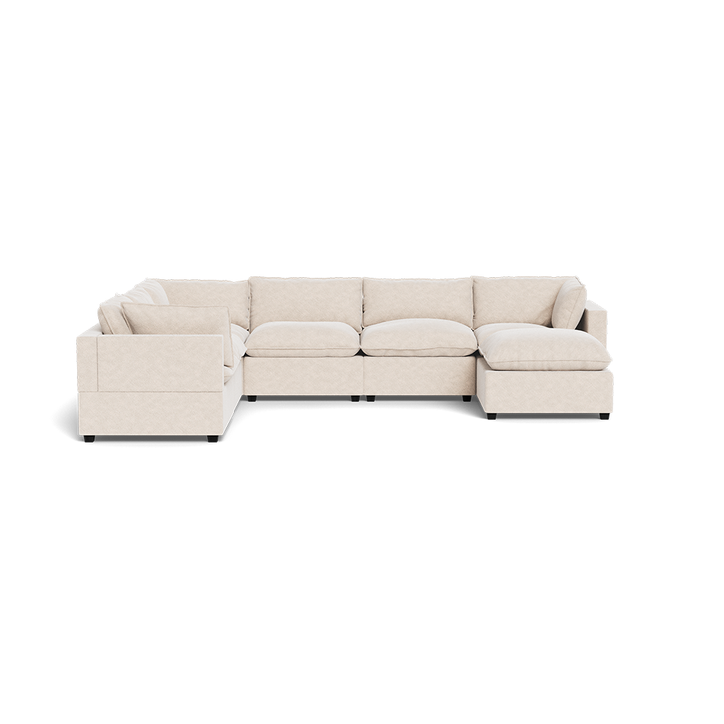 The Kova Pillow Cushion Grand Corner + Ottoman is a spacious, L-shaped sectional in light beige upholstery with deep seats, plush back cushions, and square armrests, displayed against a white background.