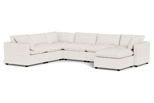 The Kova Pillow Cushion Grand Corner + Ottoman is a spacious, modern, off-white sectional sofa with plush cushions and an L-shaped design featuring a chaise lounge, shown against a plain black background.