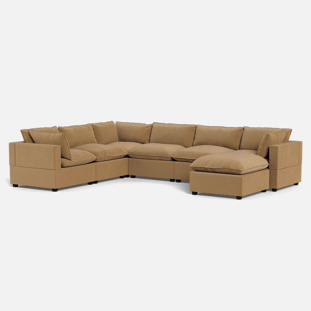 The Kova Pillow Cushion Grand Corner + Ottoman is a spacious L-shaped tan sectional with plush cushions and a chaise lounge on one end, shown against a plain white background.